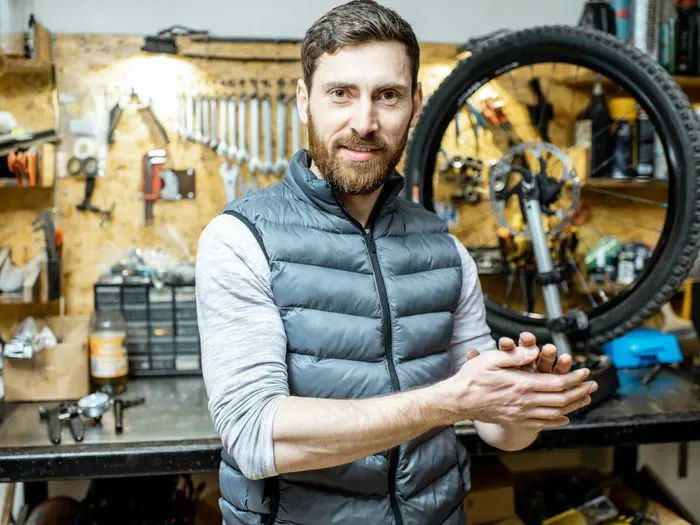 Portrait of a bicycle repair technician in a workshop with tools and wheel, representing local service listings